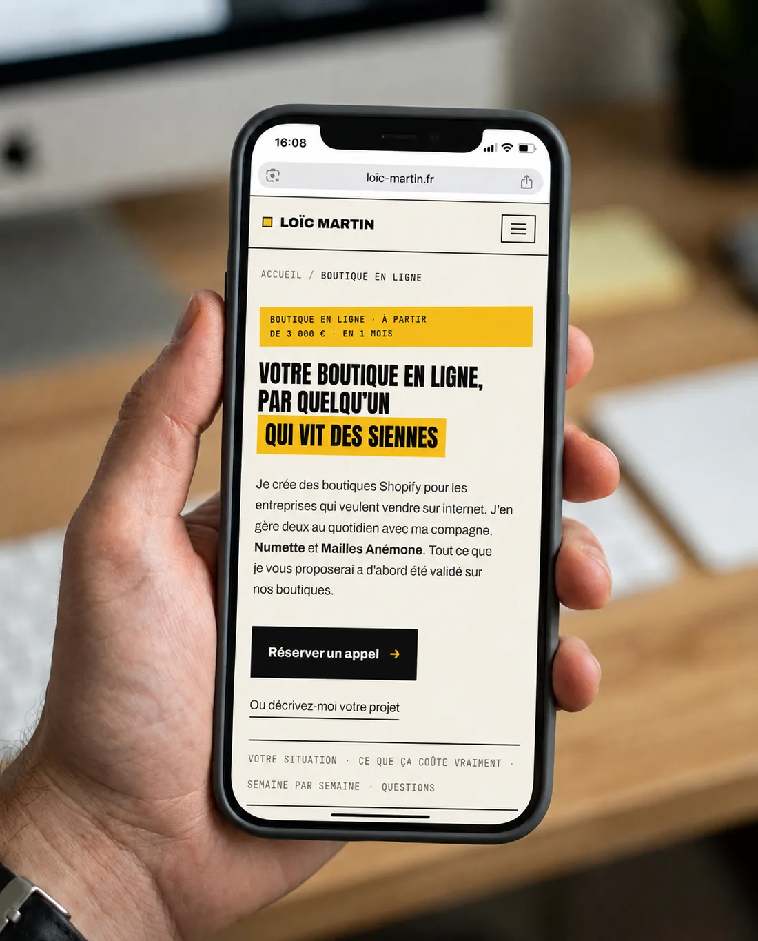 Le site loic-martin.fr ouvert sur un téléphone, tenu en main au-dessus du bureau